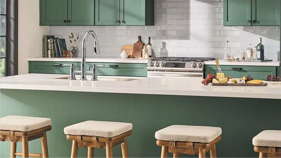 Stylish kitchen: Wooden bar stools with cream pads. Chrome Delta 3-hole faucet on green island with cream countertop. Green cabinets and cream tile backsplash in background.