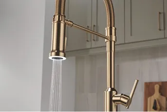 Single handle Delta Spotlight Task Light Faucet shown in champagne bronze. Water pours out. Kitchen wall with cabinets in background.
