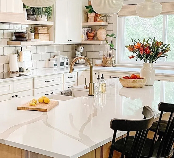 Beautifully decorated kitchen with cream cabinets, cream tile backsplash, cream kitchen island, and champagne bronze Delta faucet over double sink.