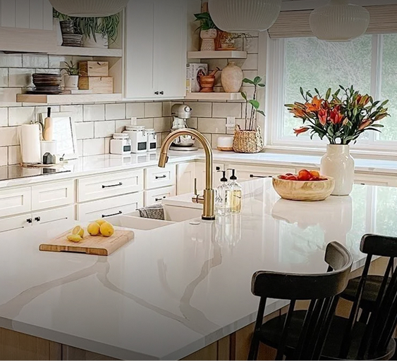 Beautifully decorated kitchen with cream cabinets, cream tile backsplash, cream kitchen island, and Champagne Bronze Delta Trinsic Single-Handle Pull-Down faucet over double sink.