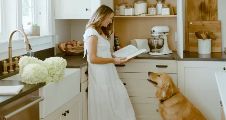 woman reads cookbook with dog in kitchen