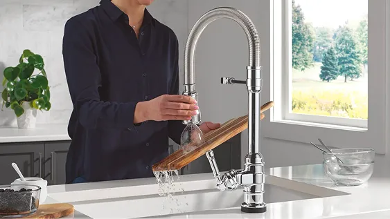 Woman in dark shirt uses spring spout spray nozzle from Delta single-handle chrome kitchen faucet to clean cutting board.