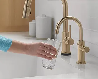 Person fills glass of water from Delta faucet in champagne bronze.