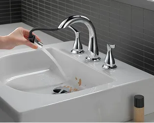 Hand uses chrome Delta Broadmoor Pulldown faucet spray nozzle to clean bathroom sink.