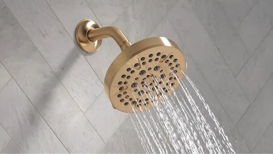 Delta Lineax shower head in champagne bronze set into grey tile wall.