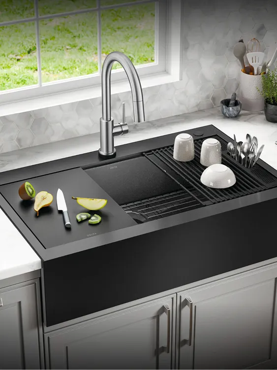 Knife, fruit slices, and clean dishes sit on Delta WorkFlow Ledge and Accessories in PVD Gunmetal on Delta Rivet Retrofit Farmhouse Apron Front 16 Gauge Workstation Kitchen Sink.