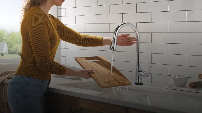Woman stands and uses Tolmac Single Handle Kitchen Pull-Down Faucet with Touchless Technology in Chrome to rinse cutting board.