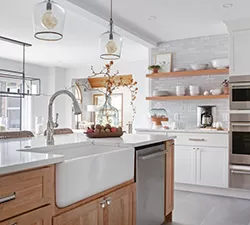 Modern kitchen with a Delta faucet installed at a deep farmhouse sink, surrounded by light countertops and neutral cabinetry.