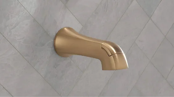 Delta Lineax bath spout in champagne bronze set into grey tile wall.